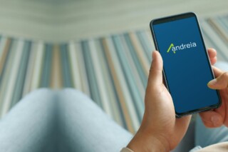 Mano che tiene uno smartphone con il logo Andreia sullo schermo, su fondo blu petrolio